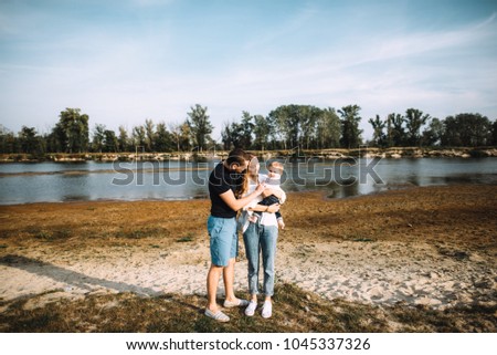 A young happy family, dad, mom and their little son, have a great time together on the nature by the river