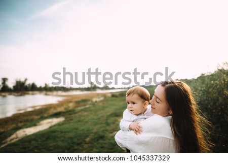 Cute little baby. Young beautiful mother is holding her baby in her arms walking with him on nature by the river