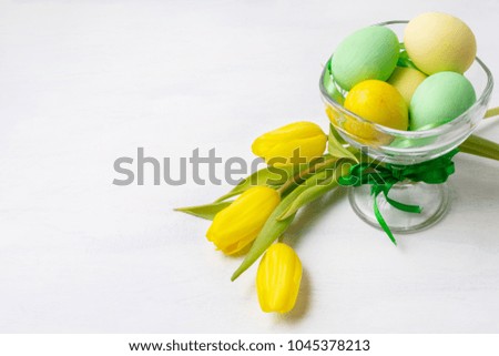 Easter background with green and yellow painted eggs in the glass vase and tulips. Happy Easter greeting card, copy space.