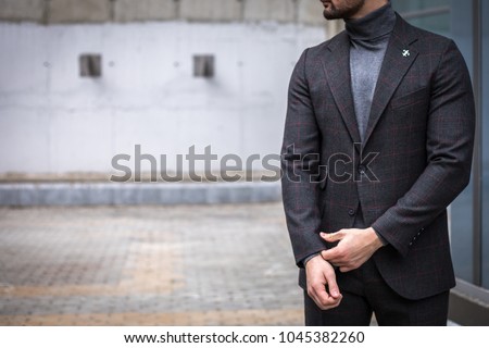 Man in custom tailored suit standing and posing outdoors while fixing his cufflinks