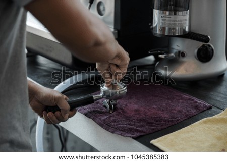 Hand of male barista holding and presses ground coffee using tamper in the workplace at cafe