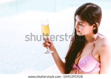 Woman wearing bikini drinking cocktail in swimming pool on summer vacation relaxing at resort spa