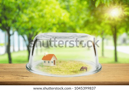 Property insurance, Toy house in glass dome on wooden floor. Shield protection Property against blurred natural on backdrop, Concept of insurance.