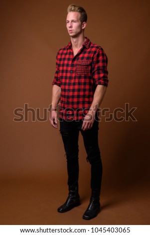 Studio shot of young handsome man wearing red checkered shirt against brown background