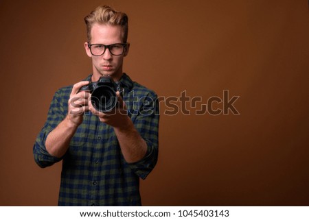 Studio shot of young handsome man wearing green checkered shirt against brown background