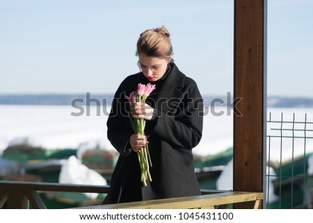 portrait of a young beautiful girl in the street in winter with tulips in a black coat