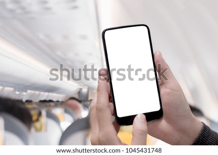 Airplane passenger using smart phone on plane with blank screen and blurred background for graphics display montage.