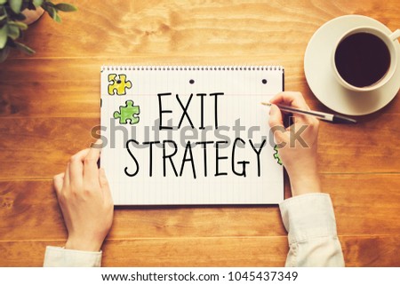 Exit Strategy text with a person holding a pen on a wooden desk