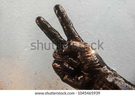 Stain hand showing peace sign with black oil on cement background.