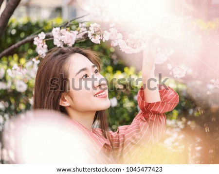 Outdoor portrait of beautiful young Chinese girl in red shirt smiling among blossom cherry tree brunch in spring garden, beauty, summer, emotion, expression and people concept.
