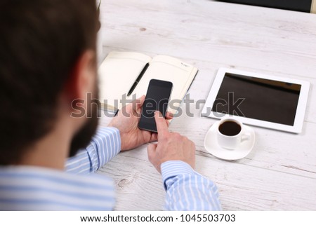 Silhouette of cropped shot of a young man working from home using smart phone and notebook computer, man's hands using smart phone in interior, 
man at his workplace using technology, flare light
