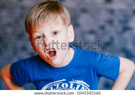 five year old boy grimaces and open his mouth in front of the camera