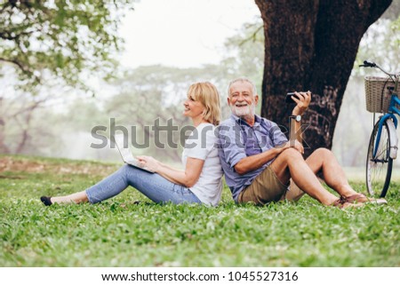 Senior couple enjoy listening to music while sitting on grass in the park