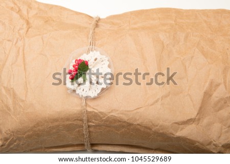 Close up view of a gift in crumpled vintage brown recycle paper tied with string and attached decoration with red berries on a white background
