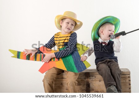 Happy caucasian kids blonde with a cardboard guitar, painted in colored colors with a microphone, sings a melodic song. Children in cowboy hats and elegant clothes for a concert on a white background