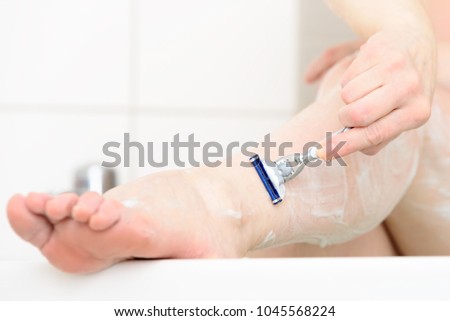Caucasian woman shaving her leg in her bathtub. Detail of leg being shaved.