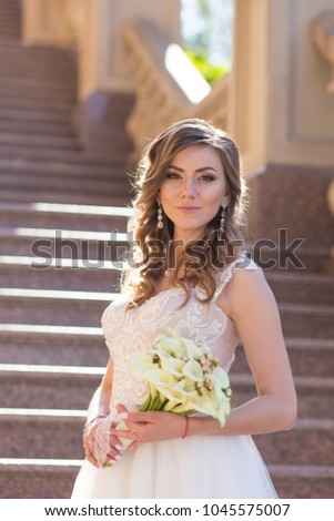 The pretty bride looks into the camera of the photographer and holds a wedding bouquet. Portrait of a beautiful bride