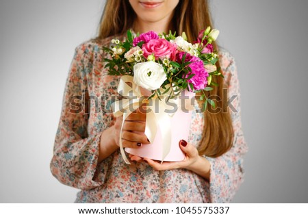 Girl holding in hand rich gift bouquet. Composition of flowers in a pink hatbox. Tied with wide white ribbon and bow.