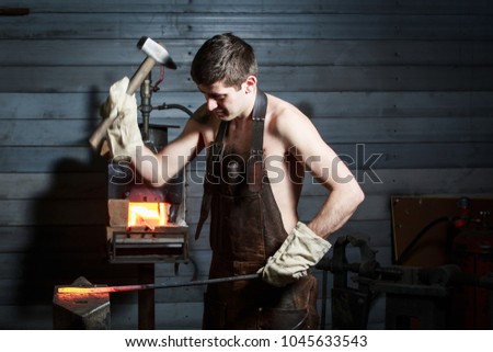portrait of a young blacksmith in a leather uniform works in a smithy