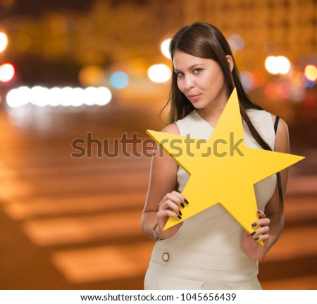 Portrait Of Young Woman Holding Yellow Star against a street background