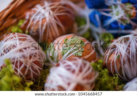Easter eggs prepared for dyeing in onions peels, decorated with natural fresh leaves, plants, rice, colorful fabric and tied with white threads. Eggs laying in wicker wooden basket full of green grass