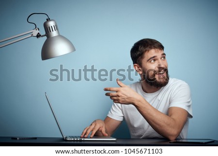  joyful man sitting at a table with a laptop on a blue background                              