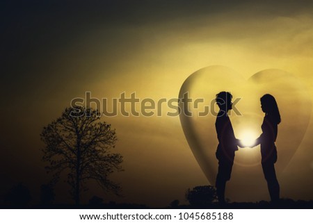 The silhouette of a man and woman standing, holding hands on evening at sunset. Have a big heart shape around there.