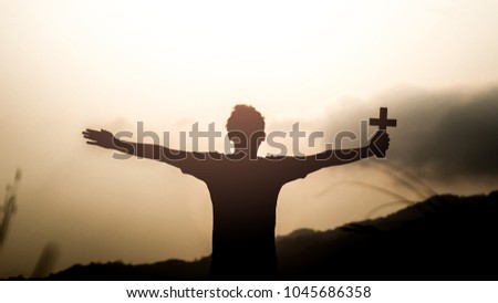 Human holding christian cross with light sunset background