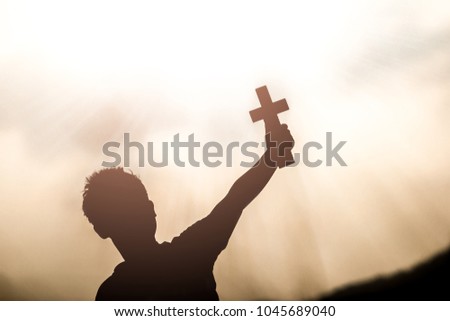 Human hand holding and lift of christian cross with light sunset background