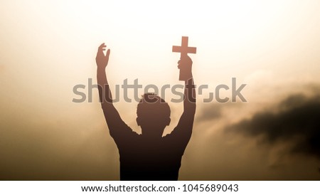 Human hand holding christian cross with light sunset background
