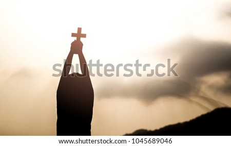 Human holding and christian cross on the head  with light sunset background