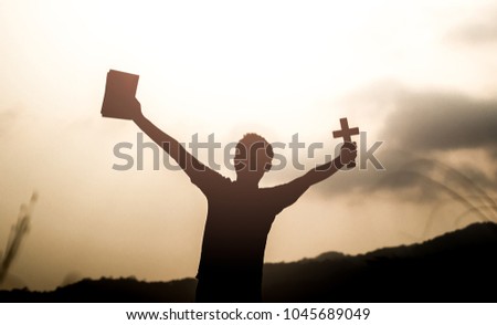Human holding Holy Bible book and christian cross with light sunset background