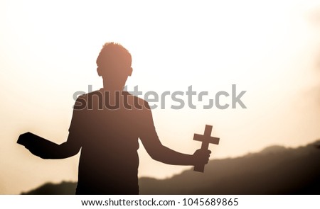 Human holding Bible book and christian cross with light sunset