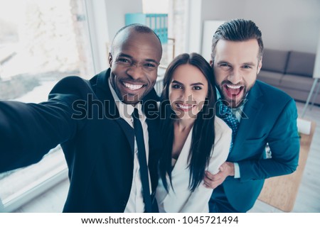 Self portrait of stylish successful, professional trio, afro-american black man with stubble shooting selfie with hand on smart phone with friends, together standing in work place, station Royalty-Free Stock Photo #1045721494