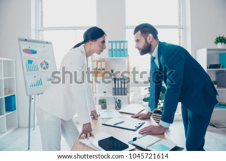 Business competition, side view profile of two colleagues in classy suits having disagreement and conflict, standing in modern work station, place, face to face, lean with hands on the table Royalty-Free Stock Photo #1045721614