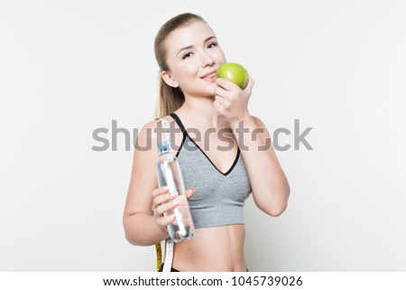 Young girl with measuring tape on shoulders holding apple and water bottle isolated on white