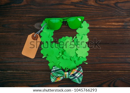 top view of bearded face symbol made of green clovers, sunglasses, blank tag and bow tie on wooden table