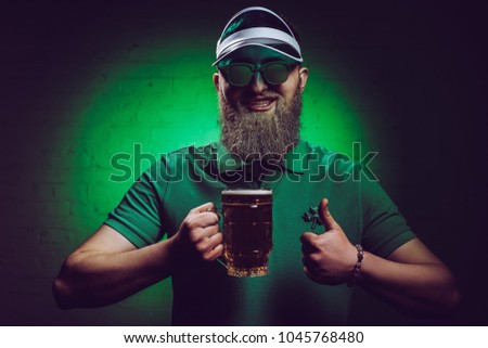smiling bearded man holding glass of beer and showing thumb up, st patricks day concept