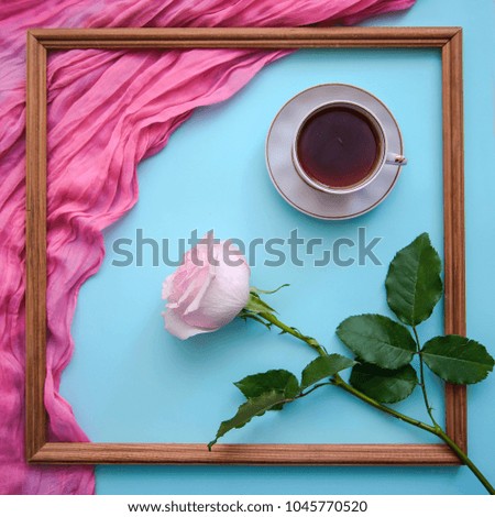Romantic picture with wooden square frame, with a cup of tea, a notebook and a pink rose on a blue background, top view