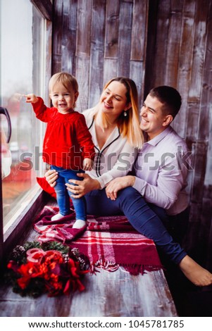 Mom and dad play with little child while she stands on the windowsill