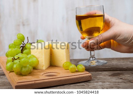 Female hand with a glass of wine, grapes and cheese