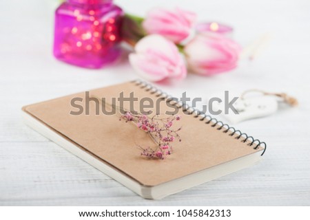 Notebook, flowers and pink lights on wooden background 