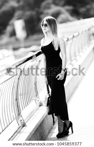Beautiful blonde girl in a black dress on a city street. Monochrome frame.