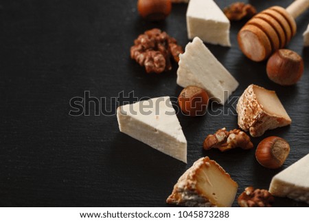 Tasting cheese with nuts on a dark stone plate. Food for wine and romantic date, cheese delicatessen on a black concrete background. Top view with copy space.