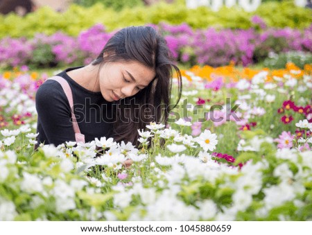 Beautiful young Asian girl in pink and black dress sitting for looking the beautiful flowers in the flowers garden.Women with nature and flower concept.