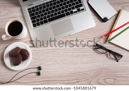 Top view of laptop and notepad with green and red color pencils, black glasses and headphones on rustic brown wood desktop and cup of hot coffee.