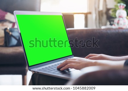 Mockup image of hands using and typing on laptop with blank green desktop screen in cafe