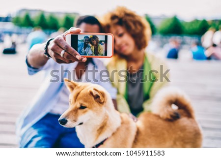 Young romantic dark skinned couple making picture on modern phone camera sitting outdoors with puppy, selective focus on picture of african american friends on smartphone doing photo with akita inu