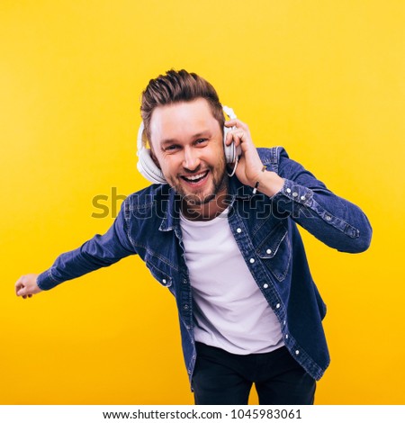 young man dancing and listening music. emotions, facial expressions, feelings, body language, signs. image on a yellow studio background.