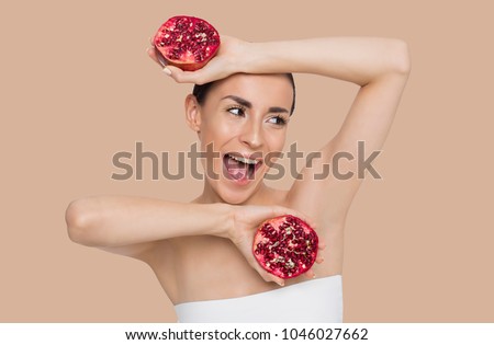 Happy and smiling beautiful woman with clean skin holding halves of pomegranate in their hands and having fun. Fruit health. Skin and body care.